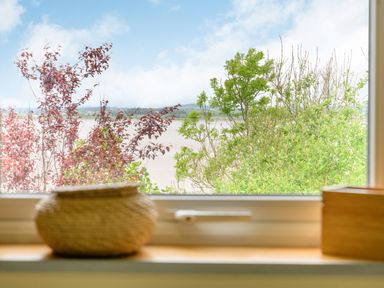 A view of trees and a river through a window with a wicker basket and a wooden box on the windowsill at Solway Cottage in Bowness-on-Solway near Wigton