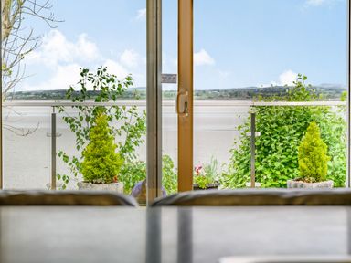A view through a glass door with plants outside and a body of water in the background at Solway Cottage in Bowness-on-Solway near Wigton