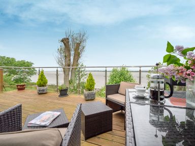 A wooden deck with outdoor wicker furniture a coffee press cups and potted plants at Solway Cottage in Bowness-on-Solway near Wigton