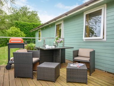 An outdoor patio with wicker chairs a table a barbecue and a small garden at Solway Cottage in Bowness-on-Solway near Wigton