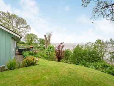 A garden with grass and bushes next to a green house overlooking a body of water at Solway Cottage in Bowness-on-Solway near Wigton