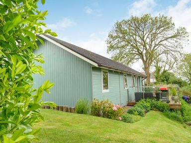A light blue house with white trimmed windows and a deck with outdoor furniture and a barbecue surrounded by grass and plants at Solway Cottage in Bowness-on-Solway near Wigton