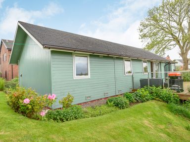 A green wooden house with a garden and patio furniture at Solway Cottage in Bowness-on-Solway near Wigton