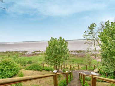 A wooden staircase leading down to a grassy area with trees and a beach beyond at Solway Cottage in Bowness-on-Solway near Wigton