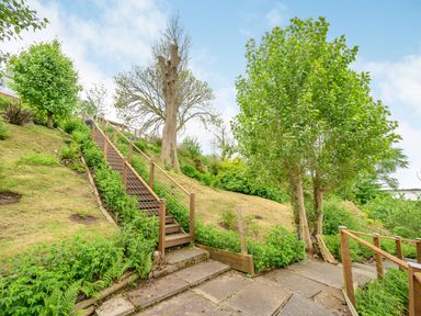 An outdoor area with wooden stairs leading up a grassy hill with trees and plants at Solway Cottage in Bowness-on-Solway near Wigton