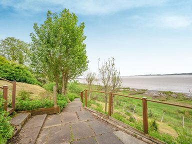 A paved pathway with stairs leading down to grassy area and mudflats by the water at Solway Cottage in Bowness-on-Solway near Wigton