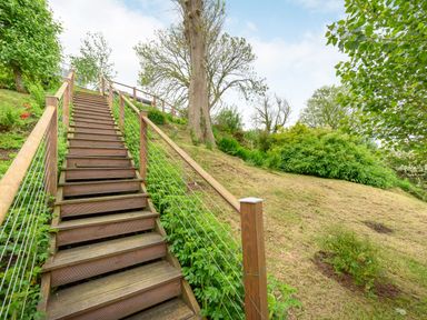 Wooden stairs with metal railing going up a grassy slope with trees and bushes at Solway Cottage in Bowness-on-Solway near Wigton