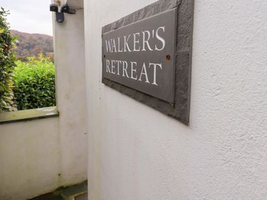 A sign reading Walkers Retreat mounted on a white exterior wall with greenery and hills in the background at Walkers Retreat in Ambleside