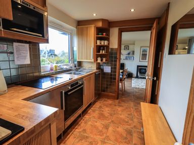 A kitchen with wooden cabinets a microwave oven a stove a sink and a door leading to a living room at Walkers Retreat in Ambleside