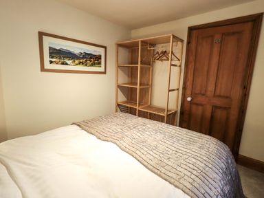 A bedroom with a bed wooden clothes rack and a framed landscape picture on the wall at Walkers Retreat in Ambleside