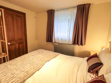 A bedroom with a bed pillows a wooden door a radiator and a window with curtains at Walkers Retreat in Ambleside