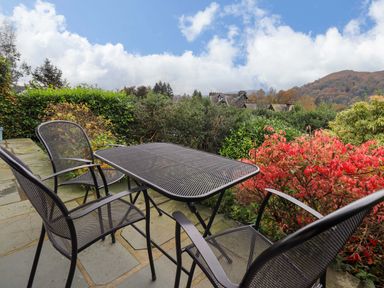 An outdoor patio with a metal table and four chairs surrounded by bushes and trees at Walkers Retreat in Ambleside