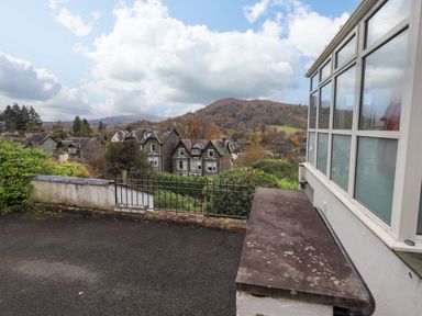 A view of houses with trees and hills in the background seen from a paved area next to a building with large windows at Walkers Retreat in Ambleside