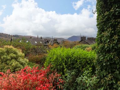 A garden with dense green and red foliage with houses and hills in the background at Walkers Retreat in Ambleside