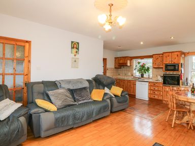 A living area with grey sofas with cushions and a kitchen with wooden cabinets and dining table at Raheen in Castletownshend County Cork