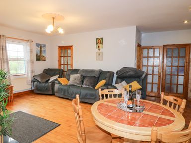 A living room with wooden chairs around a round tiled table and three sofas with cushions at Raheen in Castletownshend County Cork