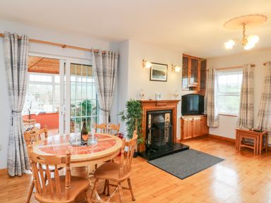 A living room with a round dining table and chairs fireplace television and large windows at Raheen in Castletownshend County Cork