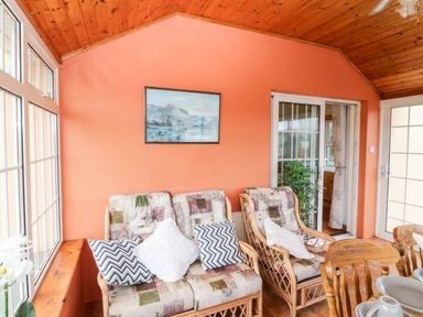 A sunroom with wicker chairs with cushions a wooden ceiling and terracotta tiled floor at Raheen in Castletownshend County Cork