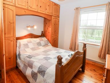 A bedroom with a wooden bed and overhead cabinets next to a window with curtains at Raheen in Castletownshend County Cork
