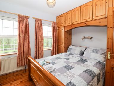 A bedroom with a wooden bed and overhead cabinets with two windows and floral curtains at Raheen in Castletownshend County Cork