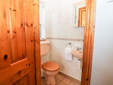 A small bathroom with a wooden door wooden toilet seat a small sink with a towel ring and a mirror above the sink at Raheen Castletownshend County Cork