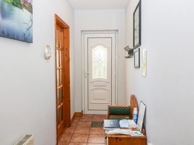 A hallway with tiled floor a white front door a wooden door a small bench with items and wall-mounted hooks at Raheen Castletownshend County Cork