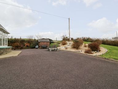 A paved outdoor area with a stone picnic table a wooden shed shrubs and a gravel path with steps leading up a small hill at Raheen in Castletownshend County Cork