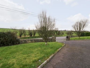 A driveway with grass and trees leading to a road with fields beyond at Raheen in Castletownshend County Cork