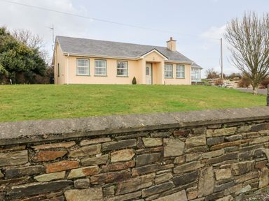 A single-story house with a sloped roof behind a stone wall and grassy lawn at Raheen in Castletownshend County Cork
