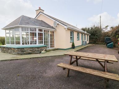 An outdoor area with a wooden picnic table and a house with a sunroom and multiple windows at Raheen in Castletownshend County Cork