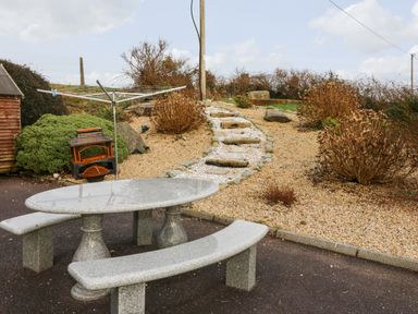 An outdoor area with a stone table and curved benches next to a gravel path with stone steps leading uphill at Raheen in Castletownshend County Cork