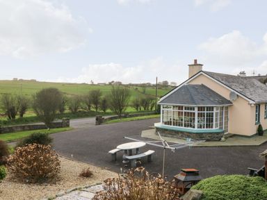 A single-story house with a conservatory and satellite dish next to a paved area with a picnic table and rotary clothesline in a rural setting at Raheen in Castletownshend County Cork
