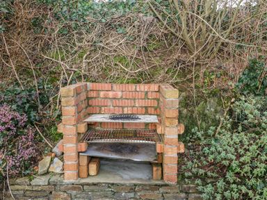 An outdoor brick barbecue grill with metal grates surrounded by plants and bushes at Raheen in Castletownshend County Cork
