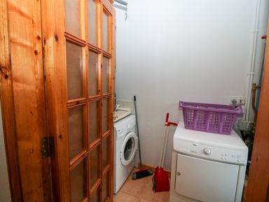 A small laundry room with a washing machine a dryer a broom and dustpan and a purple laundry basket on the dryer at Raheen in Castletownshend County Cork