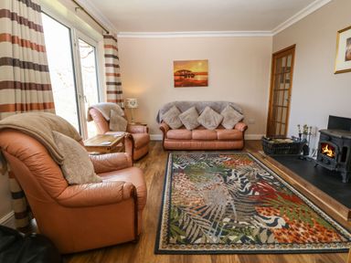A living room with leather sofas a patterned rug a wood burning stove and striped curtains at Bron Aber Arthog near Dolgellau