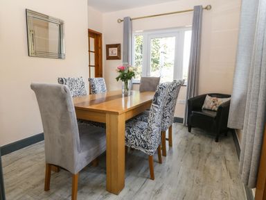 A dining room with a wooden table six chairs a vase with flowers and a black armchair with a cushion at Bron Aber in Arthog near Dolgellau