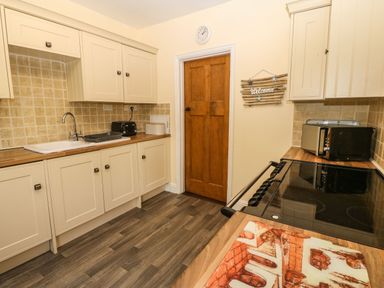 A kitchen with cream cabinets a wooden door a stove a microwave toaster and a welcome sign on the wall at Bron Aber Arthog near Dolgellau