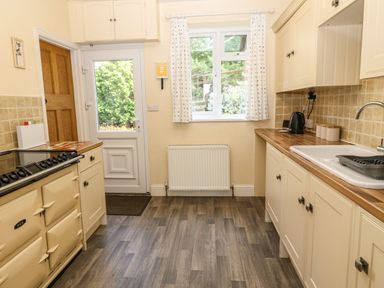 A kitchen with cream cabinets wooden countertops a stove a sink and a door with a window at Bron Aber in Arthog near Dolgellau 