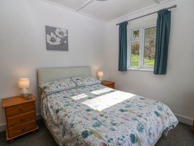 A bedroom with a double bed floral bedding two wooden nightstands with lamps and a window with blue curtains at Bron Aber Arthog near Dolgellau