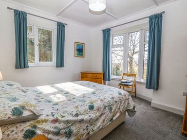 A bedroom with a bed covered in floral bedding next to blue curtains and wooden furniture at Bron Aber Arthog near Dolgellau 