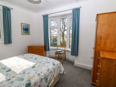 A bedroom with bed a wooden chest of drawers a wooden chair with folded towels and a window with blue curtains at Bron Aber Arthog near Dolgellau