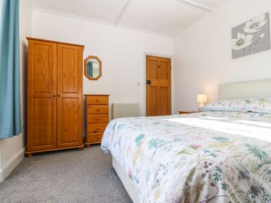 A bedroom with a double bed a wooden wardrobe chest of drawers a bedside table with lamp and floral bedding at Bron Aber Arthog near Dolgellau