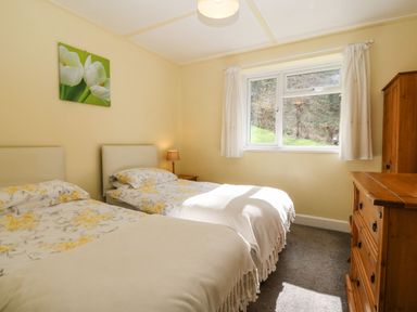 A bedroom with two single beds a wooden dresser a wooden wardrobe and a window with white curtains at Bron Aber Arthog near Dolgellau