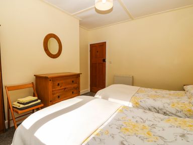 A bedroom with two beds covered in floral bedding a wooden chest of drawers a wooden chair with folded towels a round mirror on the wall and a wooden door at Bron Aber in Arthog near Dolgellau