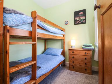 A bedroom with wooden bunk beds a chest of drawers with a lamp and folded towels at Bron Aber in Arthog near Dolgellau 