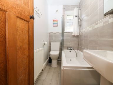 A bathroom with a wooden door a toilet a bathtub with shower and a sink at Bron Aber in Arthog near Dolgellau
