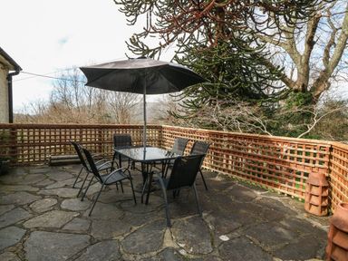 A patio with a glass table six chairs and a large umbrella surrounded by a wooden lattice fence at Bron Aber Arthog near Dolgellau