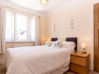 A bedroom with a bed two pillows bedside table lamp window and wooden door at Tomeg in Amble-by-the-Sea
