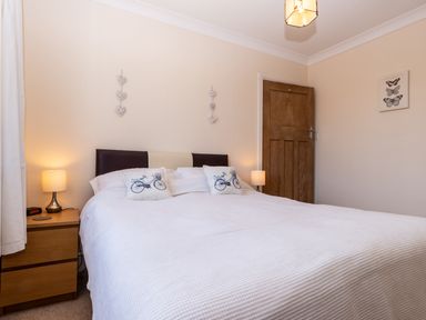A bedroom with a double bed two bedside tables with lamps and a wooden door at Tomeg in Amble-by-the-Sea