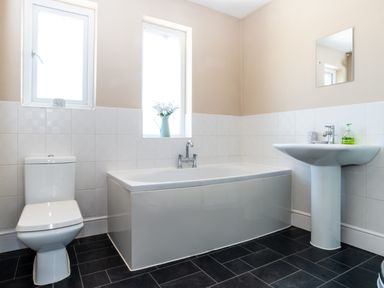 A bathroom with toilet bathtub sink and two windows at Tomeg in Amble-by-the-Sea